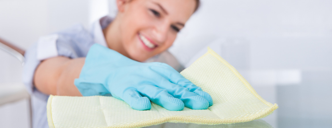 A woman wearing blue gloves and cleaning with cloth.